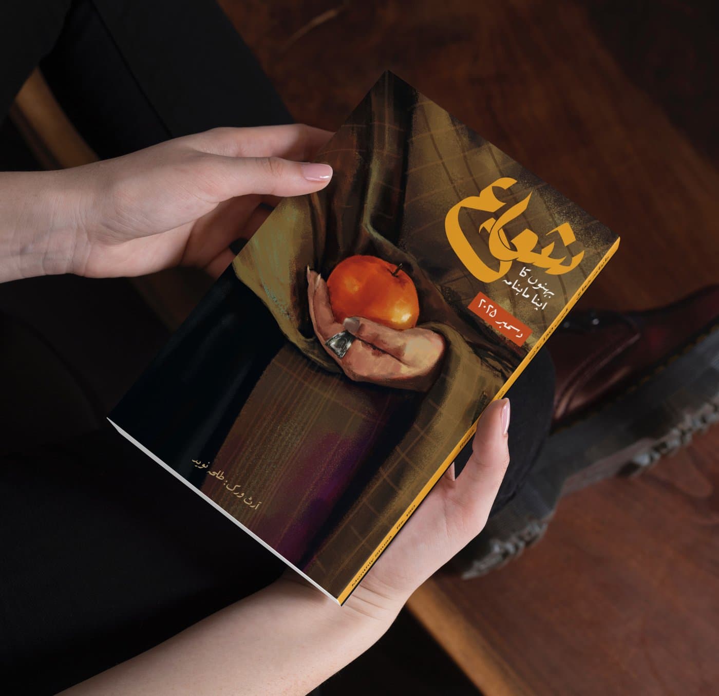 A hand holding an open issue of Shuaa Magazine on a wood table